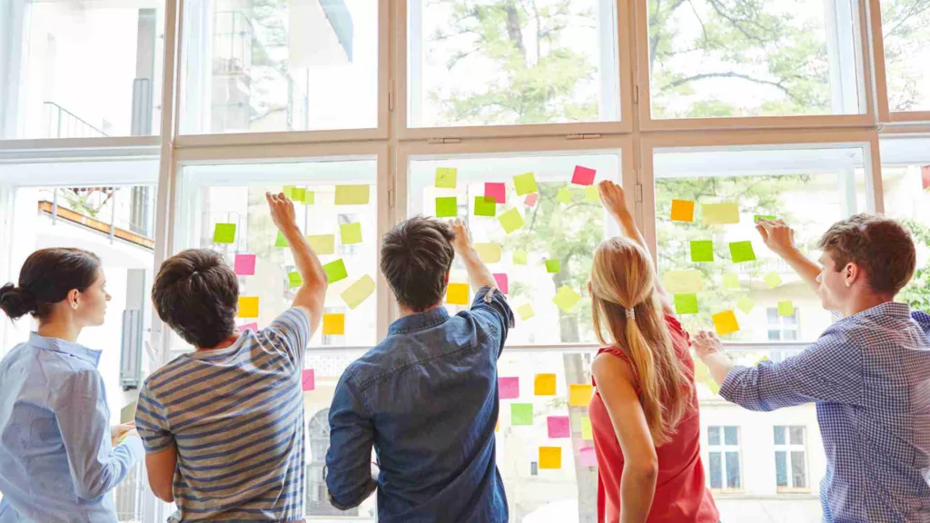 Team of people brainstorming in a meeting room, putting sticky notes onto a glass window panel