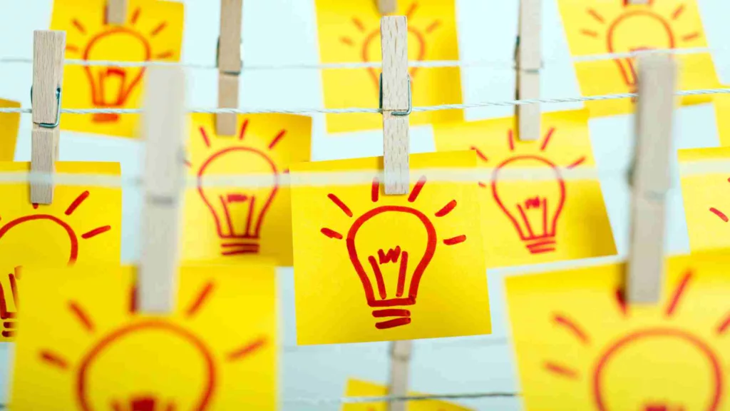 many drawings of lightbulbs, representing ideas, on yellow sticky notes, pegged to a line